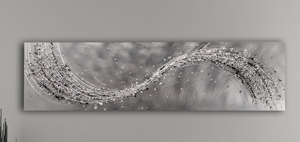 A black and white metal wall art piece with a textured surface, displayed in a modern room setting with a grey sofa and white cabinets.